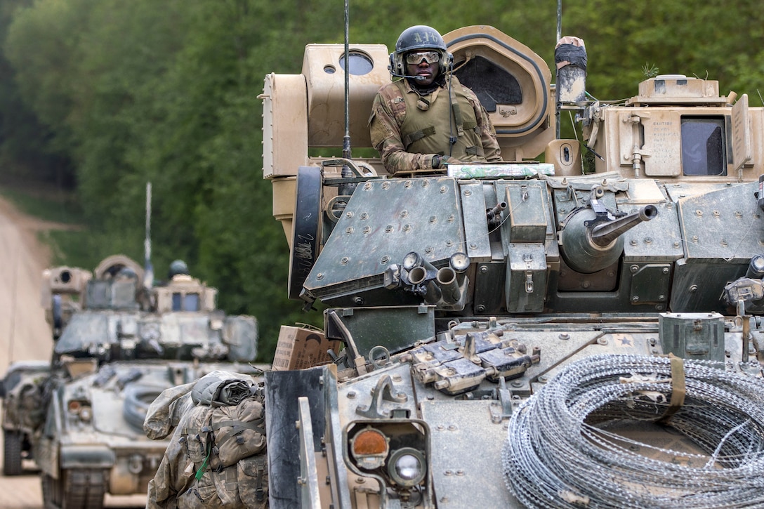 A soldier sits in a tank with another tank behind him.