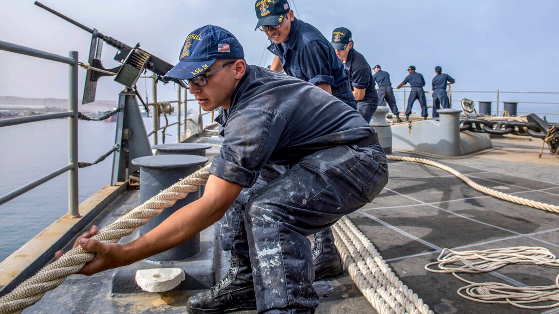 Sailors pull a rope aboard a ship.