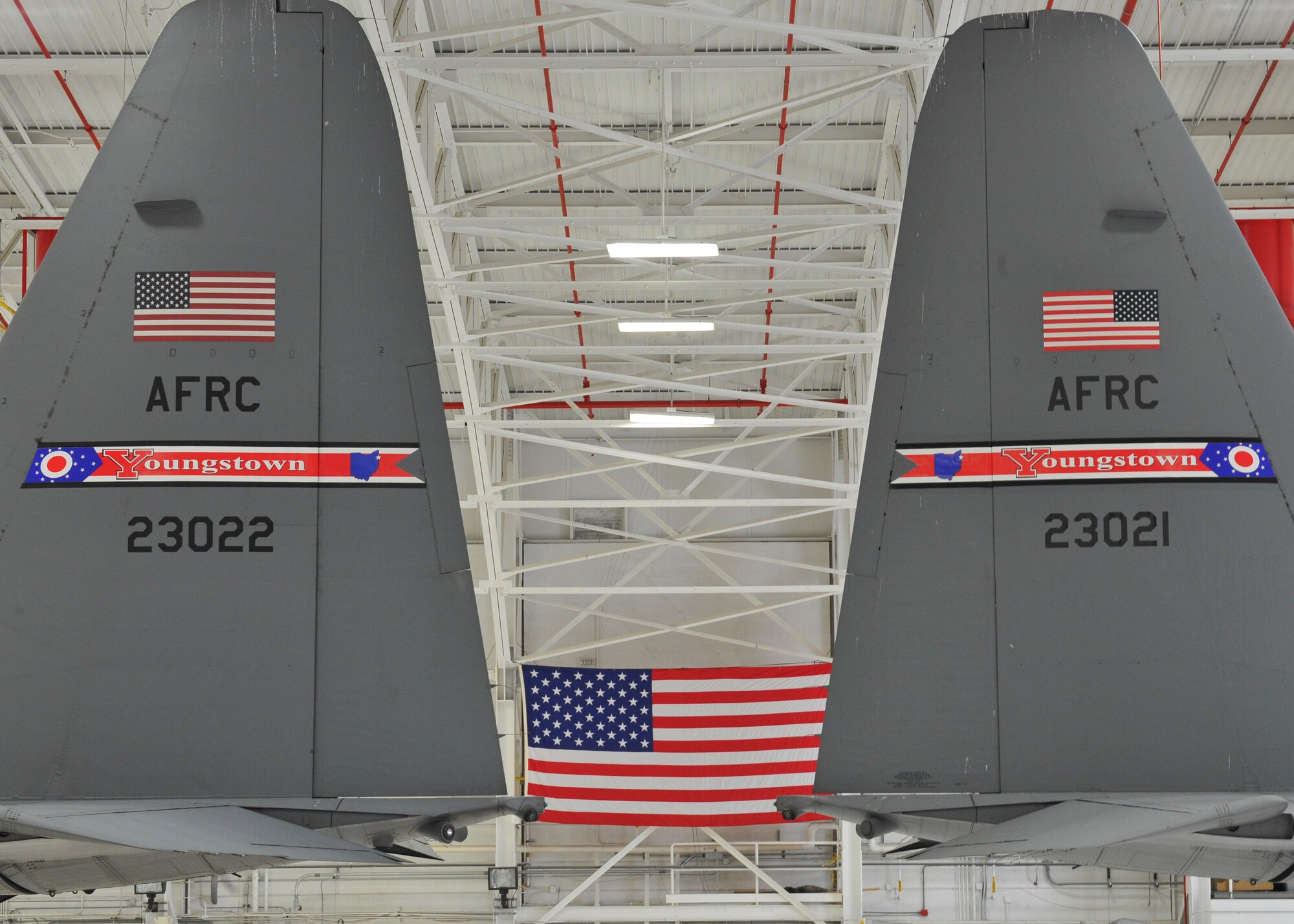 Youngstown State University President and Honorary 910th Airlift Wing Commander Jim Tressel, 910th AW Commander Col. Dan Sarachene and 910th AW Public Affairs Office Superintendent Master Sgt. Bob Barko Jr. (left to right), pose for a photo under two C-130H Hercules tails with the new tail flash design during an unveiling ceremony here May 3, 2018.