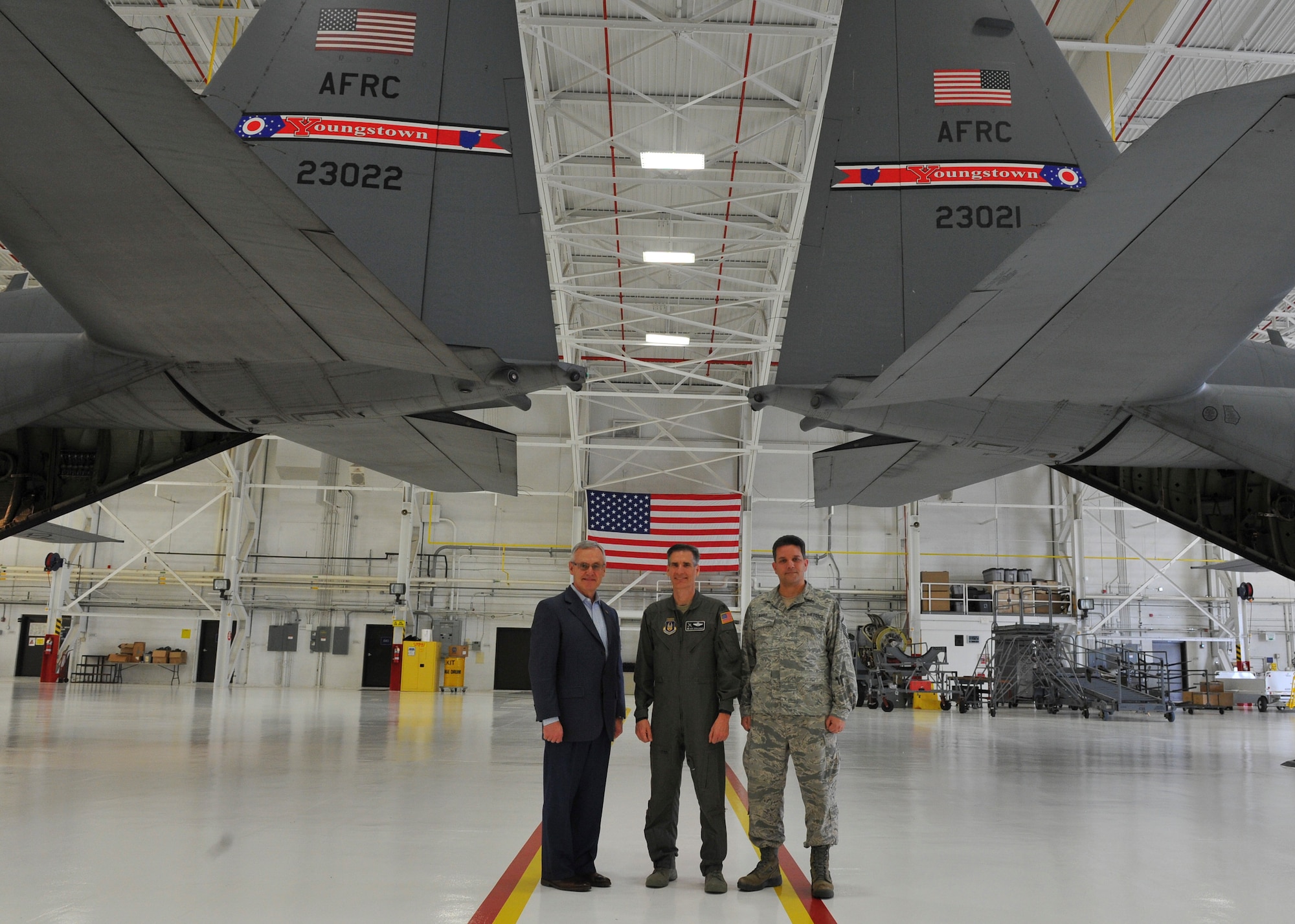 Youngstown State University President and Honorary 910th Airlift Wing Commander Jim Tressel, 910th AW Commander Col. Dan Sarachene and 910th AW Public Affairs Office Superintendent Master Sgt. Bob Barko Jr. (left to right), pose for a photo under two C-130H Hercules tails with the new tail flash design during an unveiling ceremony here May 3, 2018.