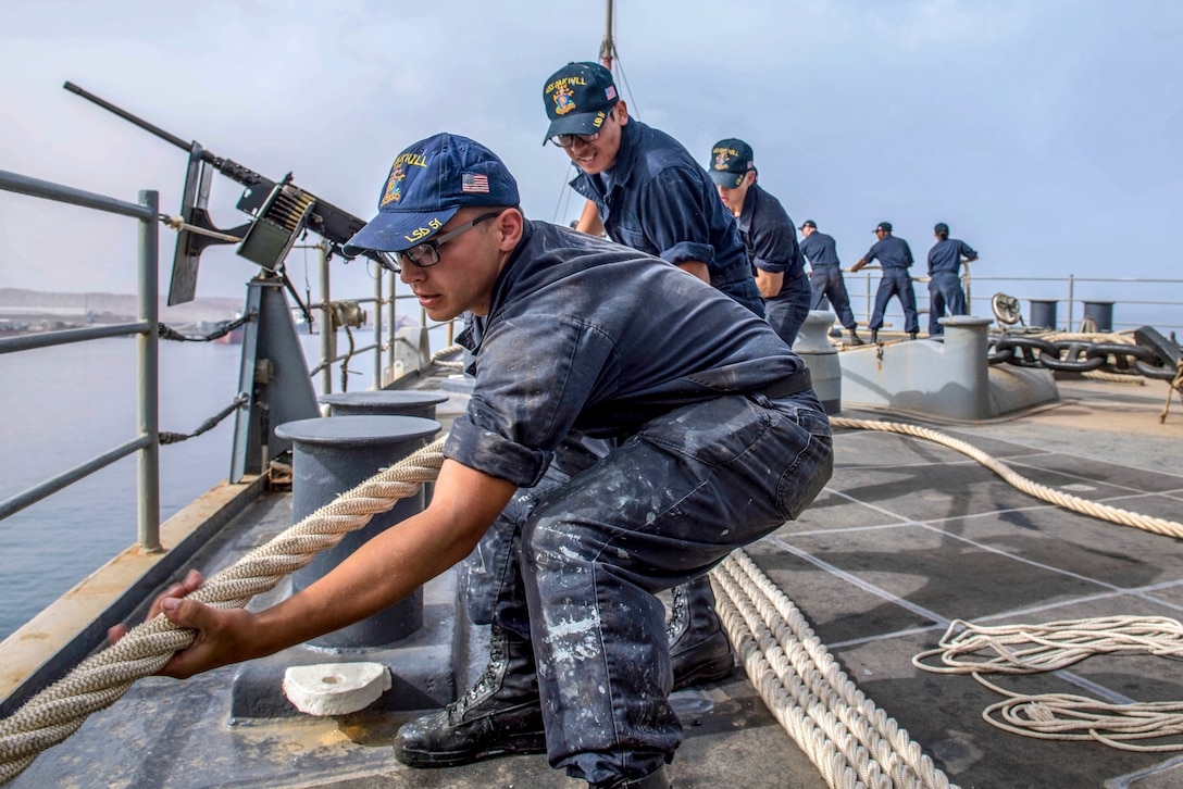 Sailors pull a rope aboard a ship.