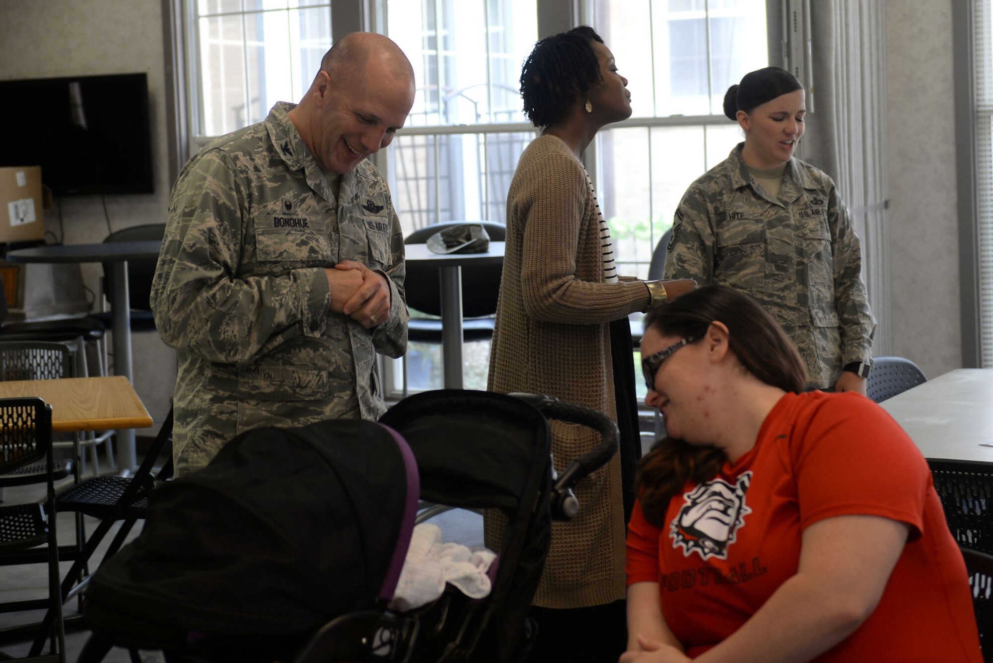 A man in the Airman Battle Uniform looks into a stroller next to a woman in a red shirt looking in the stroller.