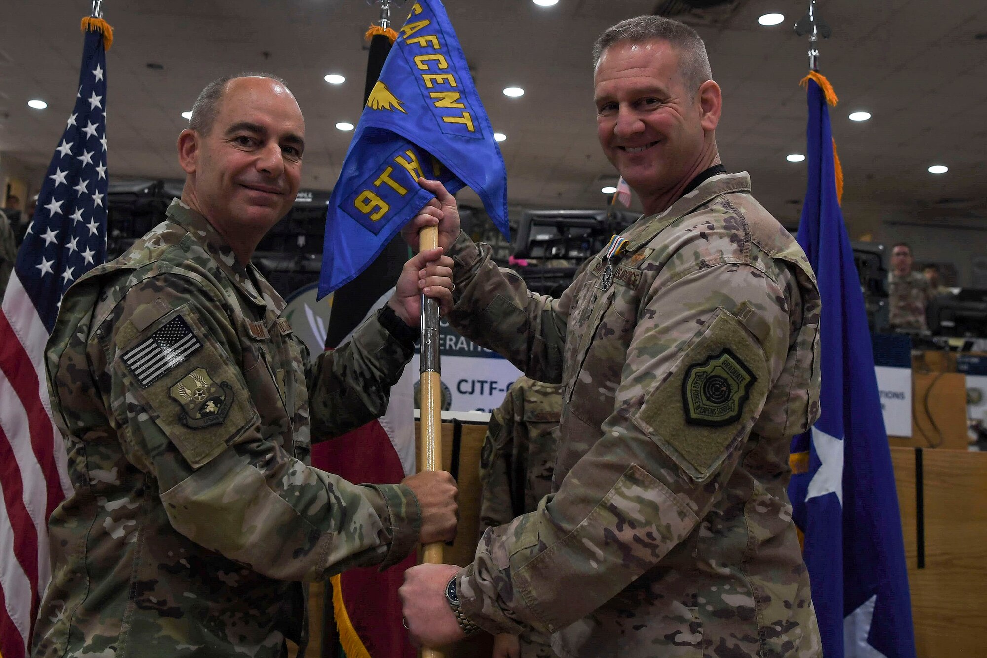 Maj. Gen. Dirk Smith (right), 9th Air Expeditionary Task Force - Levant outgoing commander, passes the 9th AETF-L guidon to Lt. Gen. Jeffrey Harrigian, United States Air Force Central Command commander, during a change of command ceremony May 5, 2018, at an undisclosed location in Southwest Asia.