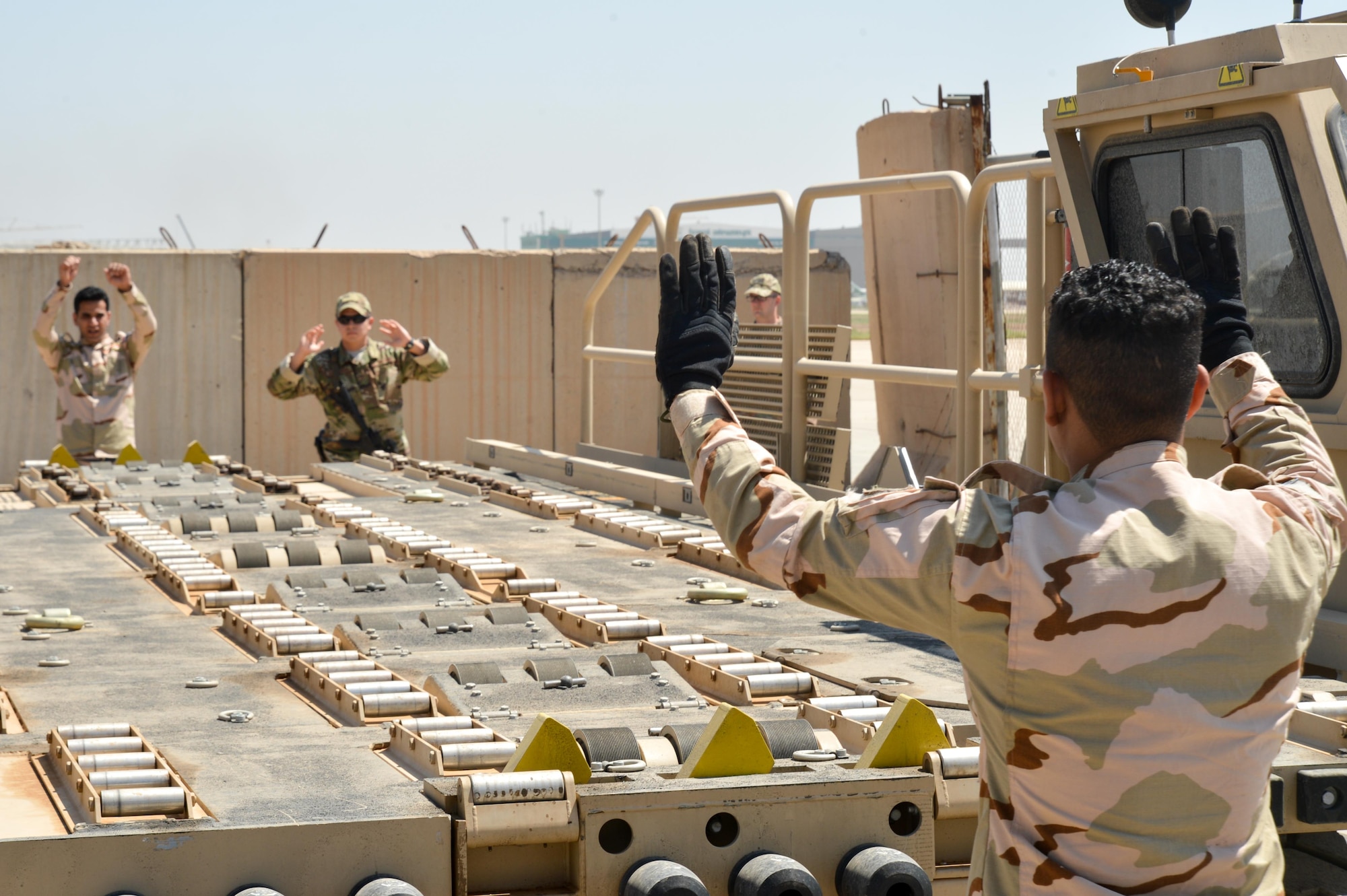 Senior Airman Juan Calderon, 370th Air Expeditionary Advisory Group air advisor (back right) works with Iraqi Air Force airmen as they back up a K-Loader, at Al Muthana Air Base, April 23, 2018. Air advisors work with their Iraqi counterparts to assist with training and safety protocols specific to their expertise. (Air Force photo by Staff Sgt. William Banton)