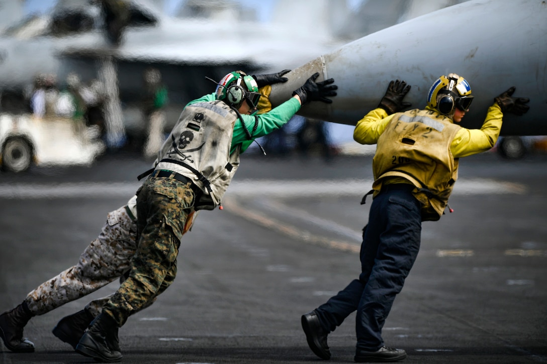 Marines and a sailor push an F/A-18C Hornet on the flight deck.