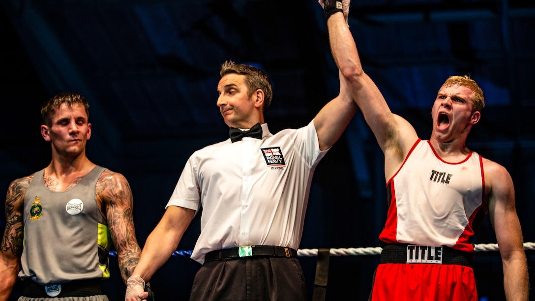 A referee stands between two boxers, raising the arm of the one, who shouts in victory, and holding the arm of the other down.