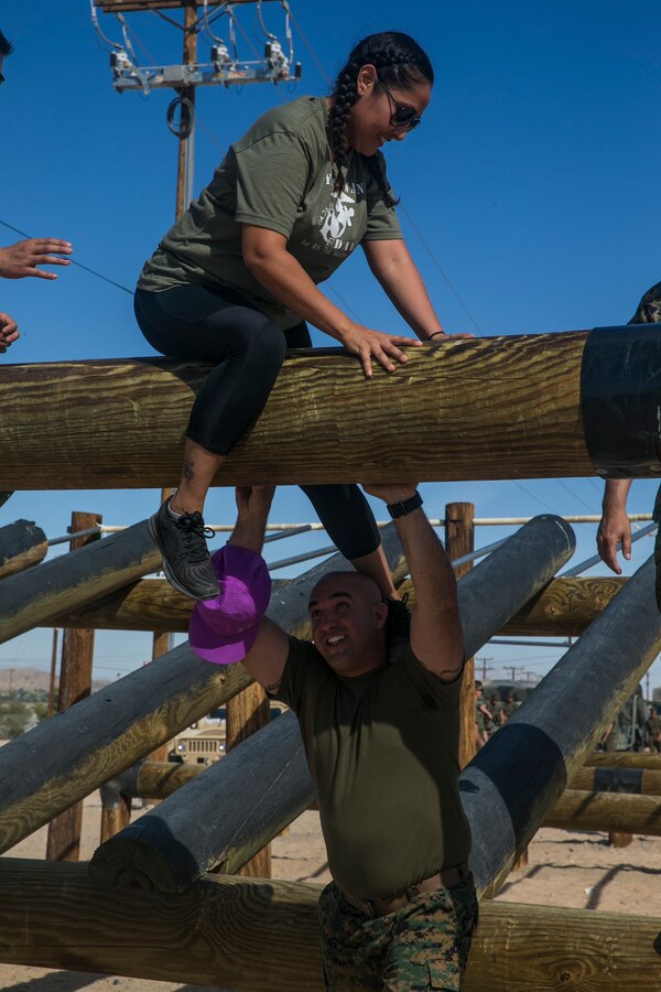 1st Sgt. Gilbert Oshana, company company first sergeant, 1st Battalion, 7th Marine Regiment, helps his wife Elda Oshana, over a log obstacle at the obstacle course during the unit's Jane Wayne Day aboard the Marine Corps Air Ground Combat Center, Twentynine Palms, Calif., April 27, 2018. This Jane Wayne Day gave the spouses a glimpse into the day-to-day lives of their active duty spouses through an obstacle course, a live-fire range and different battle simulations. (U.S. Marine Corps photo by Lance Cpl. Dave Flores)