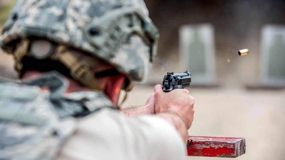 A bullet flies from a pistol as an airman, shown from behind, fires toward a target on a range.