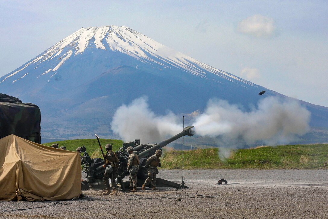 Marines fire a howitzer, with Mount Fuji in the background.