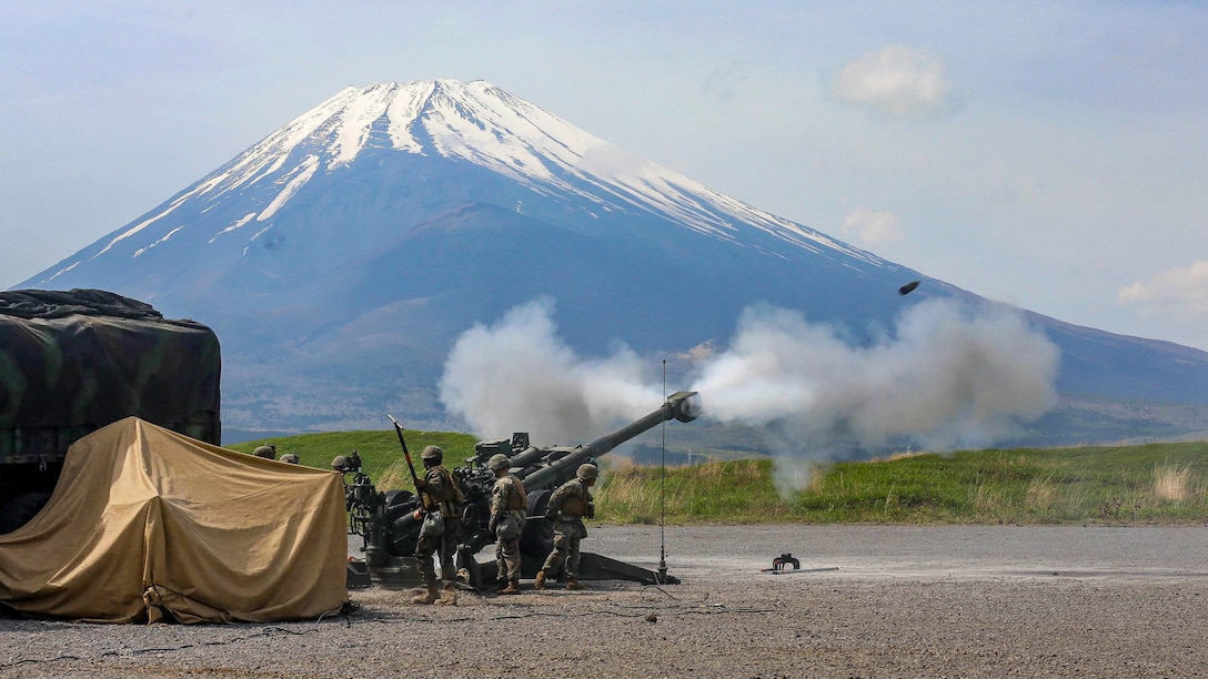 Marines fire a howitzer, with Mount Fuji in the background.