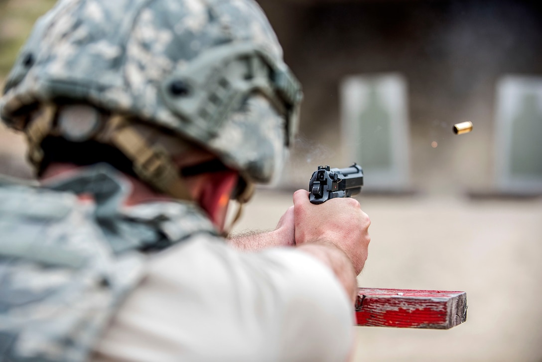 A bullet flies from a pistol as an airman, shown from behind, fires toward a target on a range.