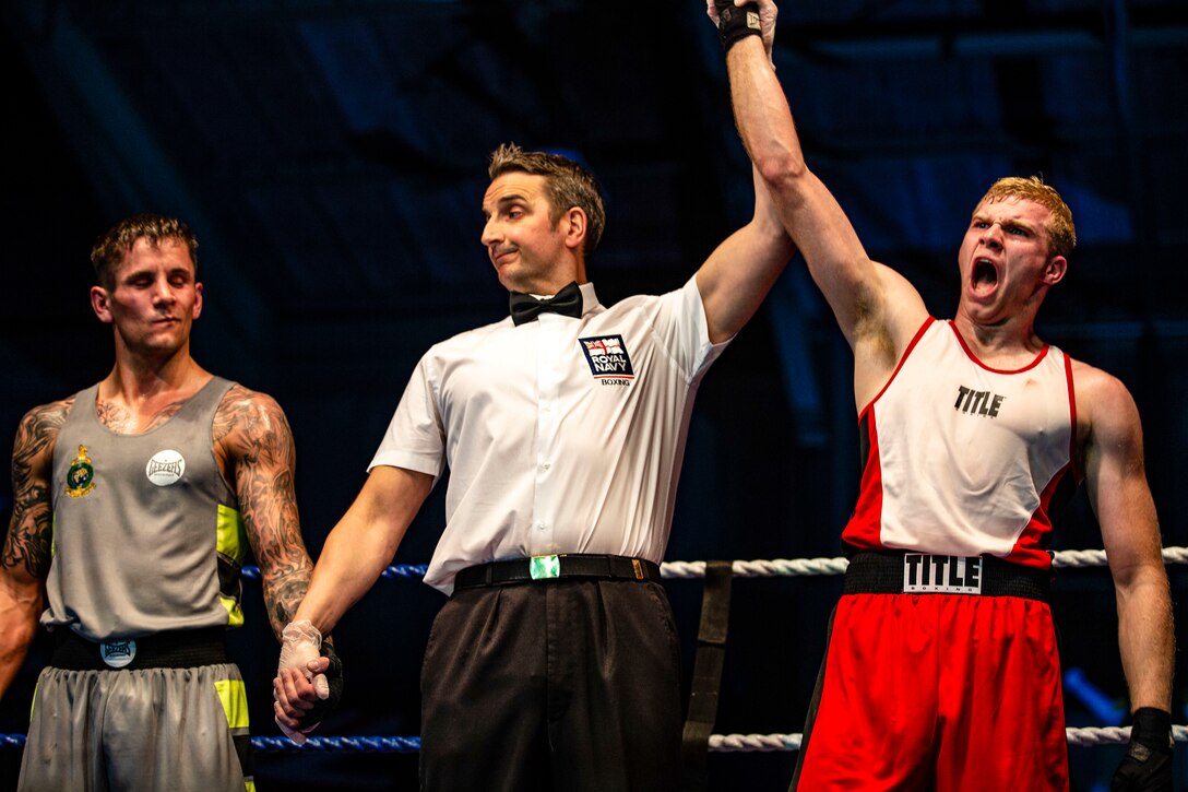 A referee stands between two boxers, raising the arm of the one, who shouts in victory, and holding the arm of the other down.