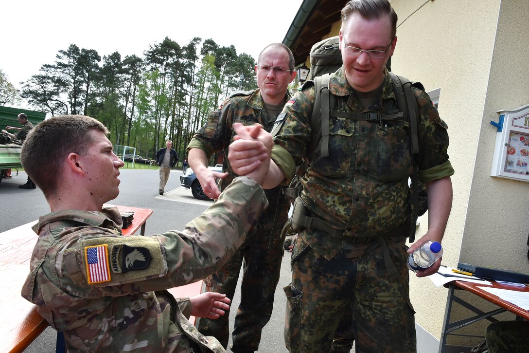 A German and a U.S. soldier shake hands after completing a ruck march.