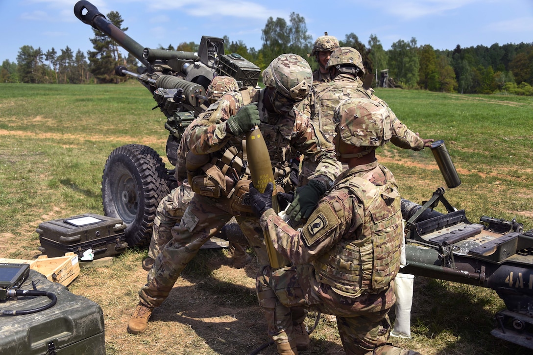Soldiers prepare to load a round into an M119 105mm howitzer.