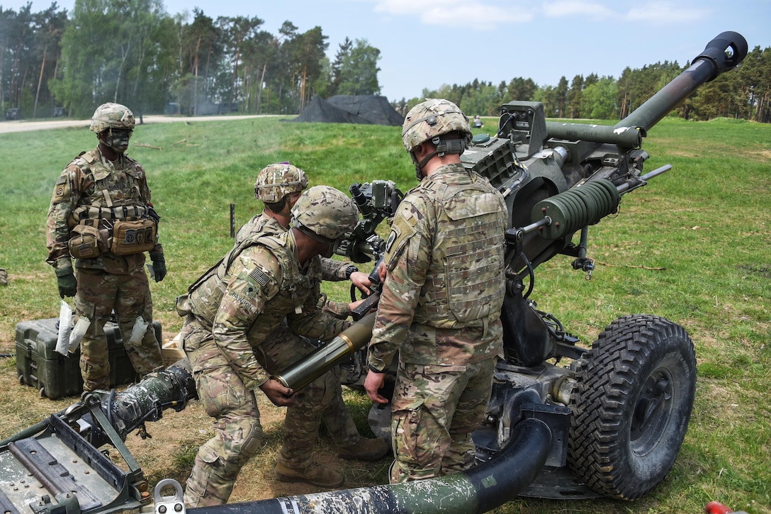 Soldiers load a round into an M119 105mm howitzer.