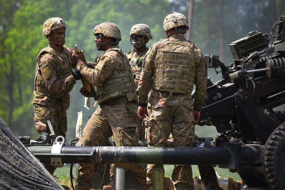 Soldiers handle ammo while loading an M119 105mm howitzer.