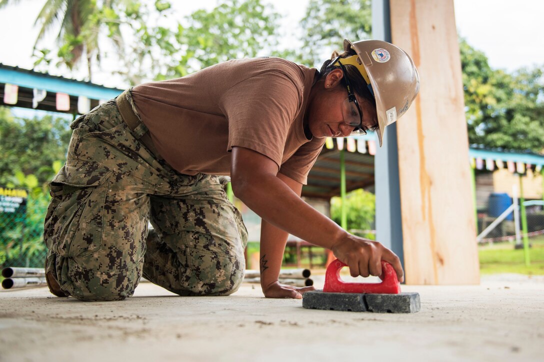 A sailor removes material from a concrete floor.