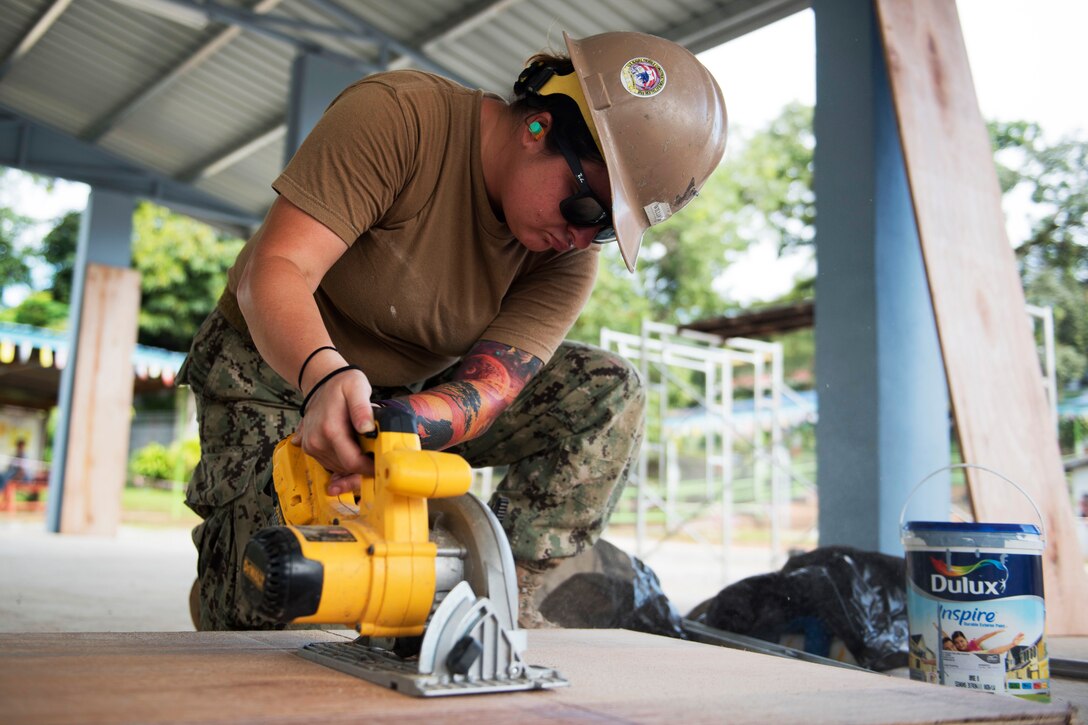 A sailor cuts roofing materials at an engineering project.