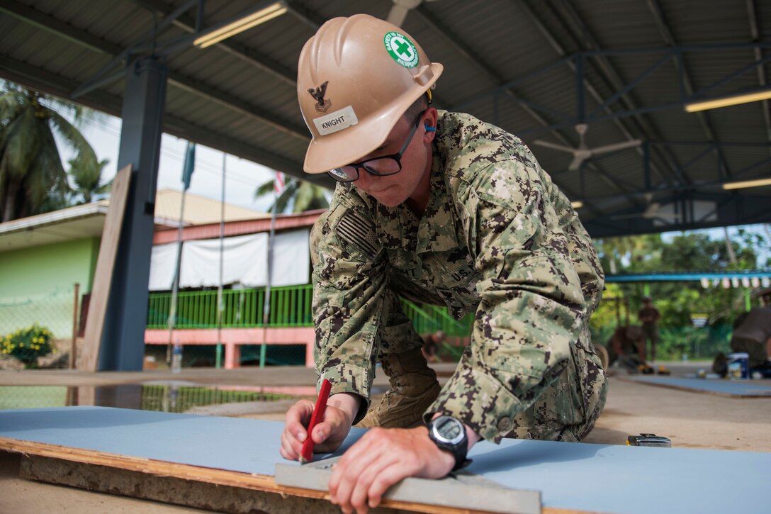 A sailor takes measurements of roofing materials.