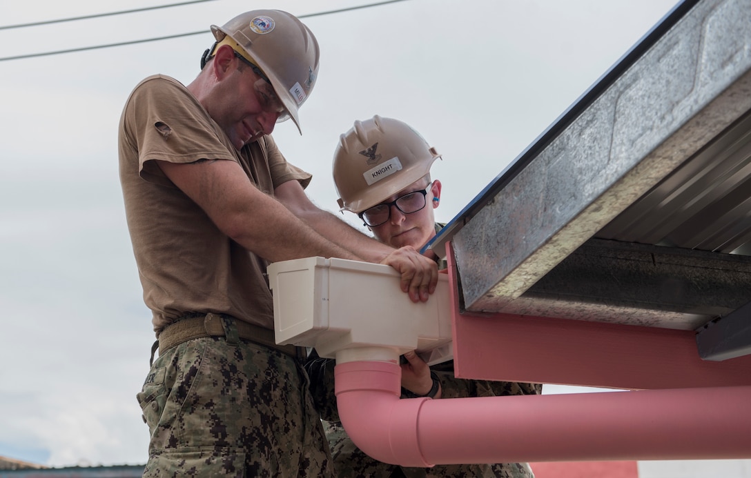 Navy sailors install a rain gutter.