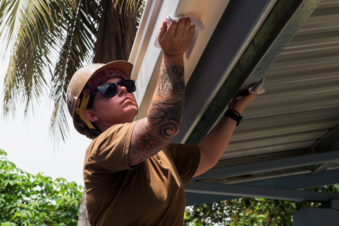 A sailor cleans a rain gutter at the project site.