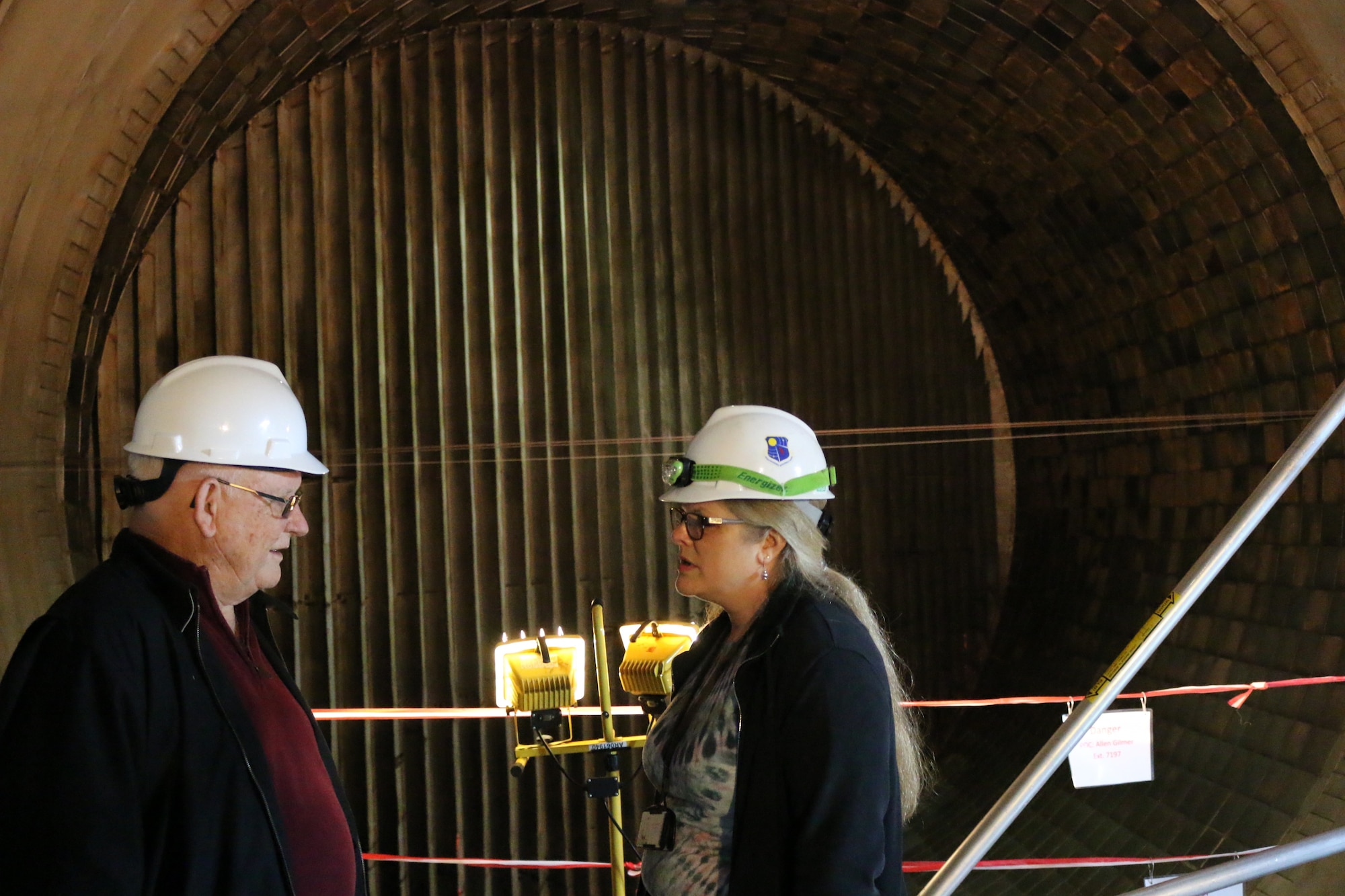 With the wind tunnel itself serving as the backdrop, AEDC retiree Bill Comer, left, discusses the early days of Propulsion Wind Tunnel 16S with engineer Valerie Davenport, a member of the core engineering team assigned to the 16S Return to Service project. Comer was one of eight retirees who recently visited Arnold Air Force Base to offer their input and knowledge as current employees work to return to 16S to service. (U.S. Air Force photo/Bradley Hicks)