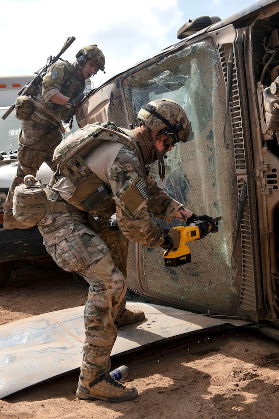 An airman uses a power saw to cut through the windshield.