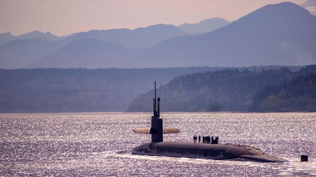 A submarine travels in water with mountains in the background, all of which have a purplish tint.