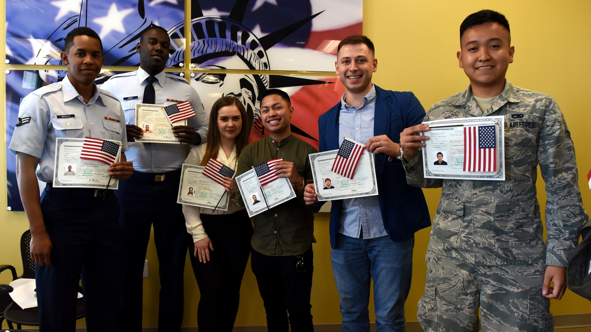 Individuals stand in front of a wall with a mural of the American flag for a group photo