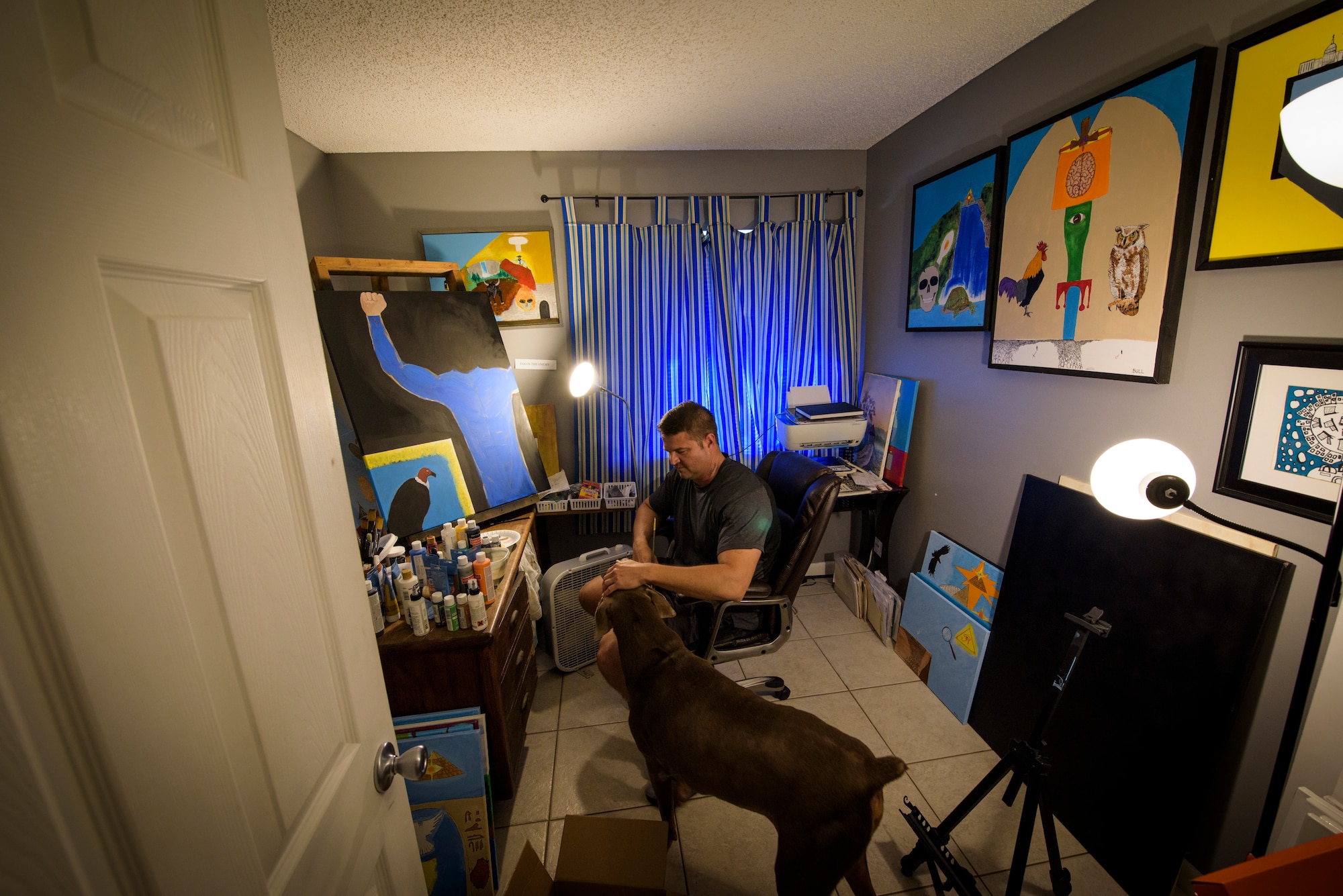 Officer Tim Bull, a Combat Arms Training and Maintenance instructor, pets his dog, Harley, in between painting, April 24, 2018, in Palm Bay, Fla. Bull is an artist and turned to art as an outlet and release. Bull has a unique art style that combines the surreal with earnest, thought provoking messages. "It took me 37 years to find out what I wanted to do and this is it" (U.S. Air Force photo by Airman 1st Class Dalton Williams)