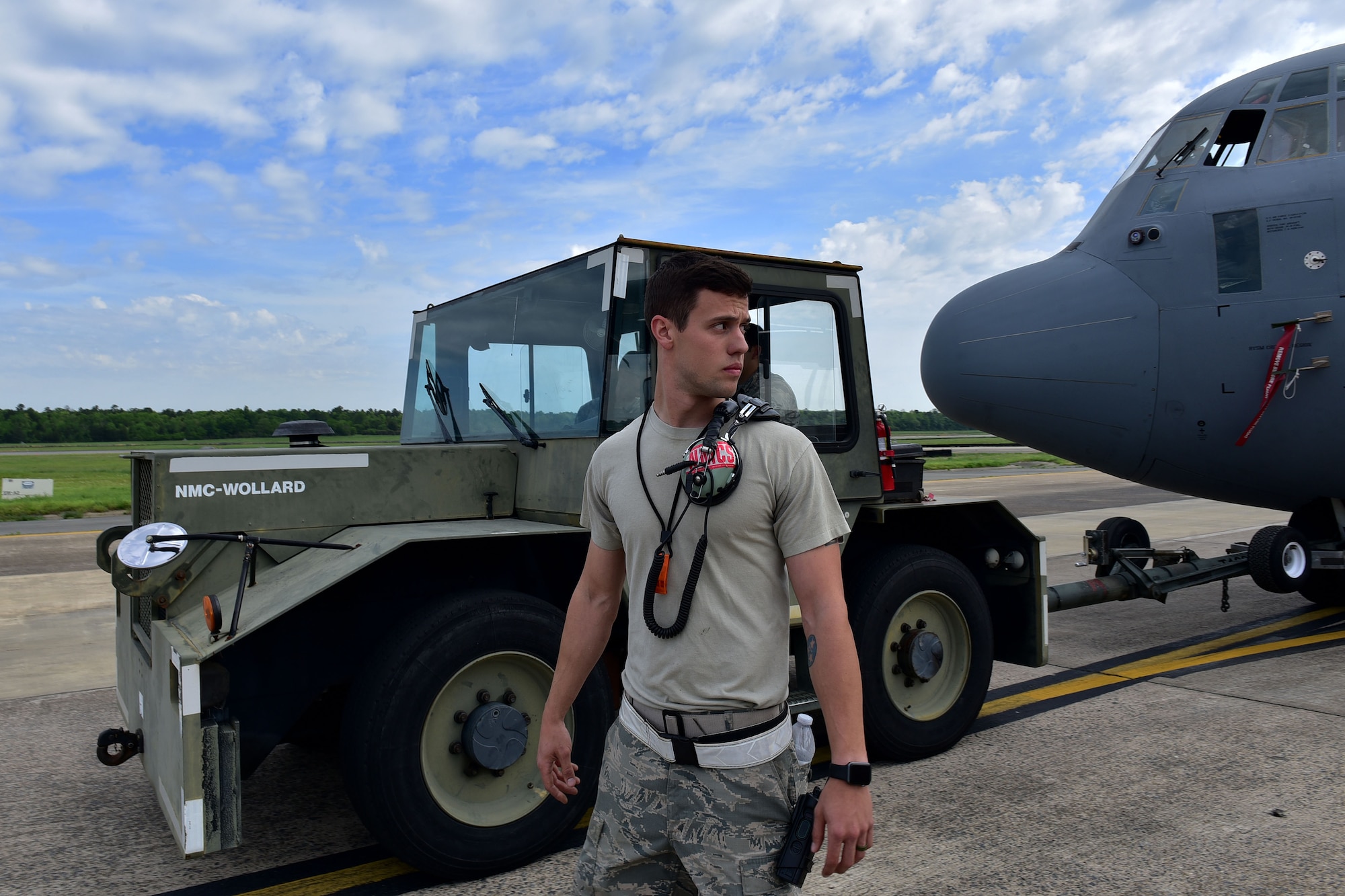 A man walks with a tow tractor towing a C-130J.