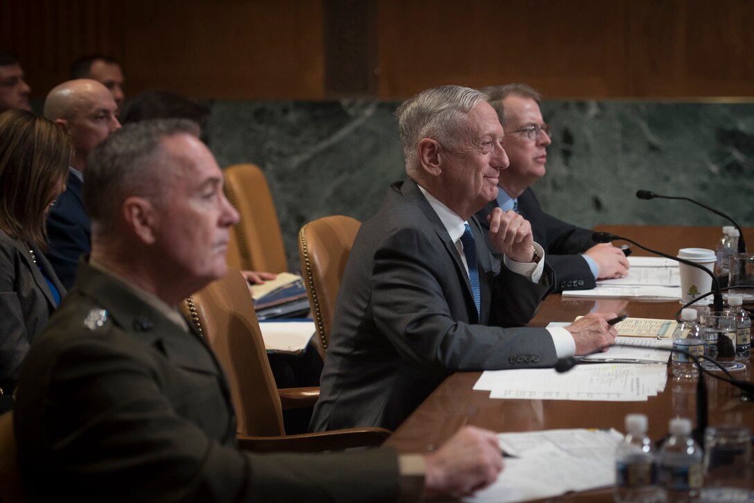 Defense Secretary James N. Mattis, the comptroller and the chairman of the Joint Chiefs of Staff sit behind a desk.