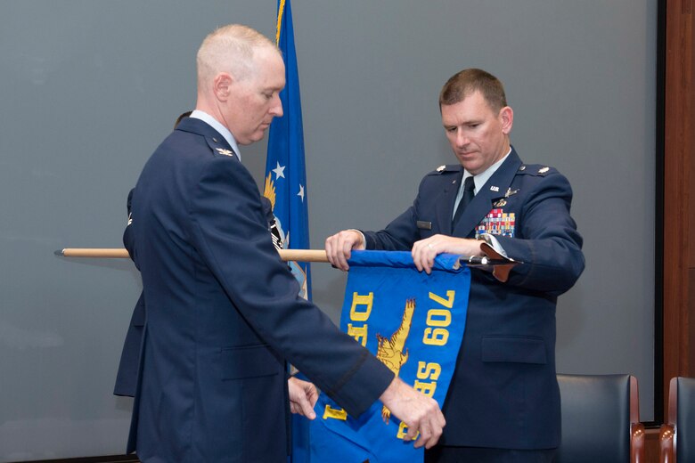 Col. Richard Mendez (left), 709th Support Group commander, assists Lt. Col. David Laird, commander of the group’s Detachment 1, unfurl the unit’s new guidon flag during a ceremony held April 6, 2018 at Patrick AFB, Fla.  Laird took command of the detachment as part of the Air Force Technical Applications Center’s reorganization to improve mission effectiveness.  (U.S. Air Force photo by Matthew S. Jurgens)