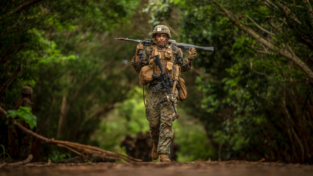 A Marine carries a machine gun on his shoulders in a forest.