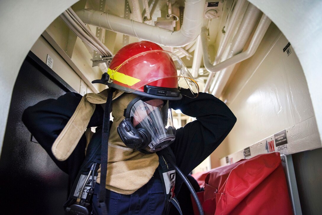 A sailor dons a firefighting helmet.