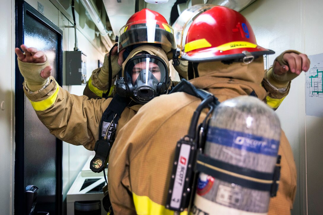 Sailors help each other don firefighting gear.