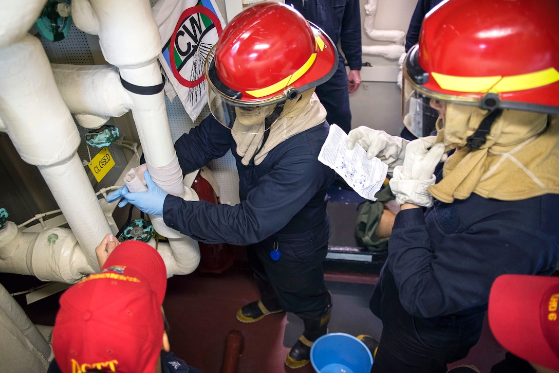 Sailors apply an emergency water-activated patch to a pipe.