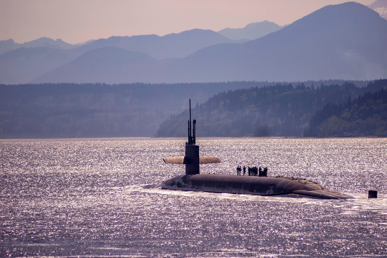 A submarine travels in water with mountains in the background, all of which have a purplish tint.