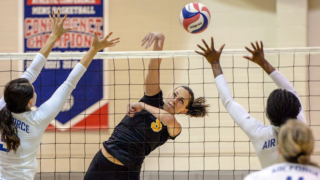 A soldier spikes a volleyball as airmen on the other side of the net raise their arms.