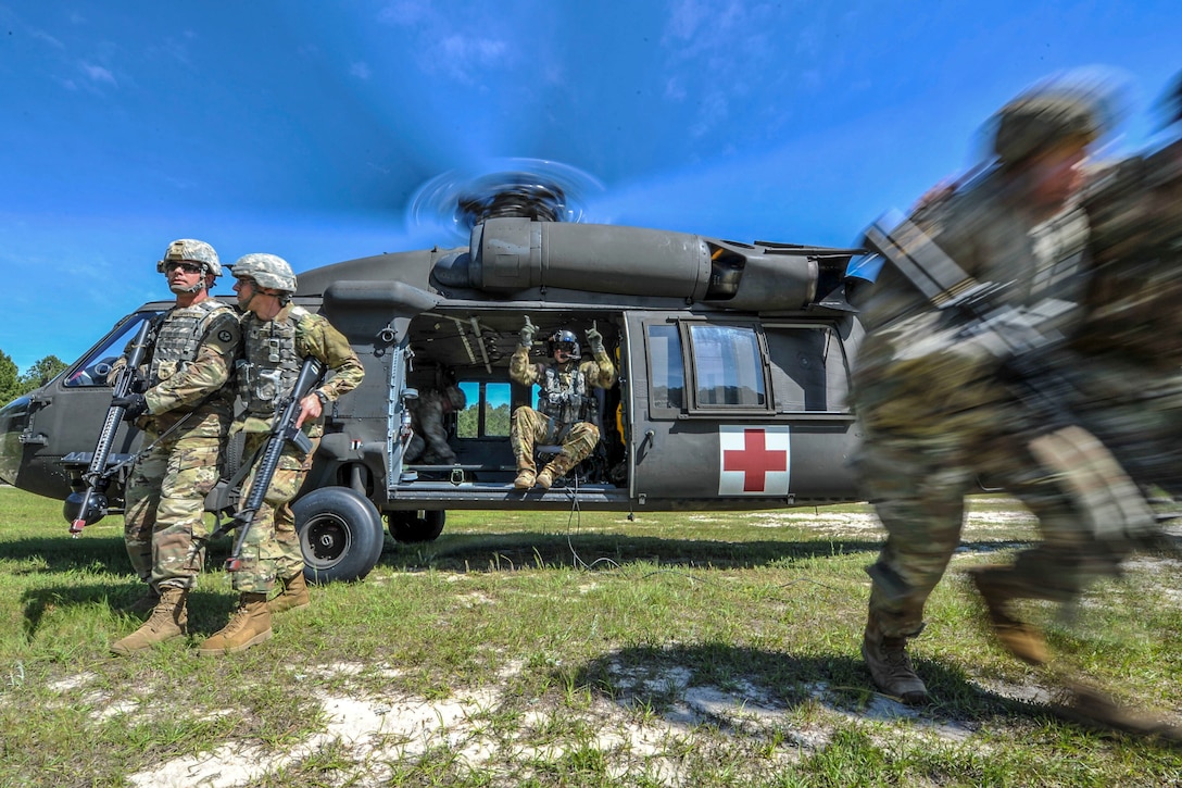 Soldiers run from a helicopter idling in a field, as a soldier sitting in the copter points instructions.