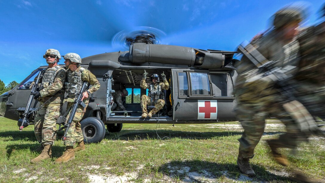 Soldiers run from a helicopter idling in a field, as a soldier sitting in the copter points instructions.