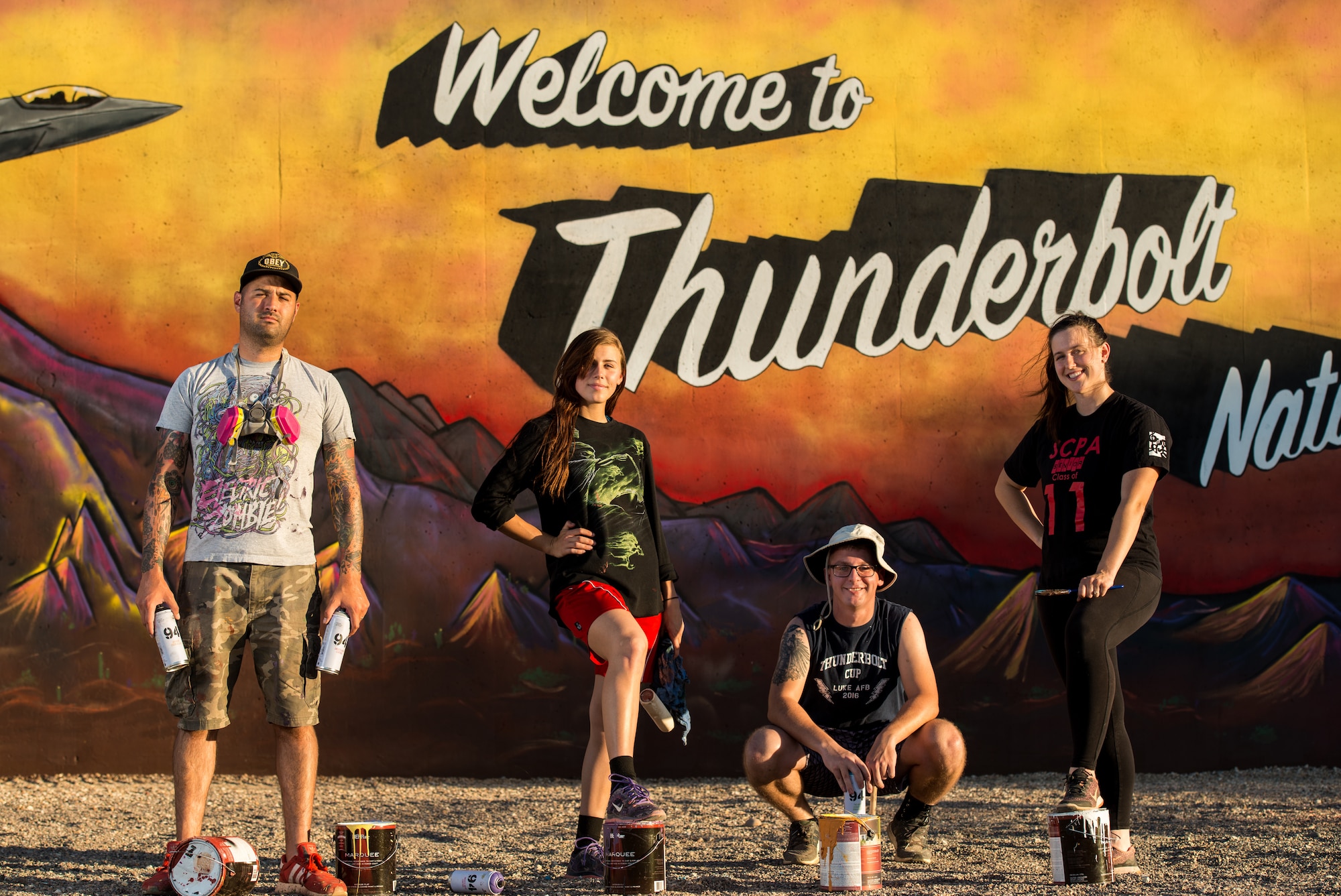 The team of Thunderbolt artists pose for a group photo in front the “Welcome to Thunderbolt Nation” mural at Luke Air Force Base, Ariz., May 9, 2018. Over the course of a month, the team worked together to complete the mural, which represents Luke’s heritage. (U.S. Air Force photo by Airman 1st Class Alexander Cook)