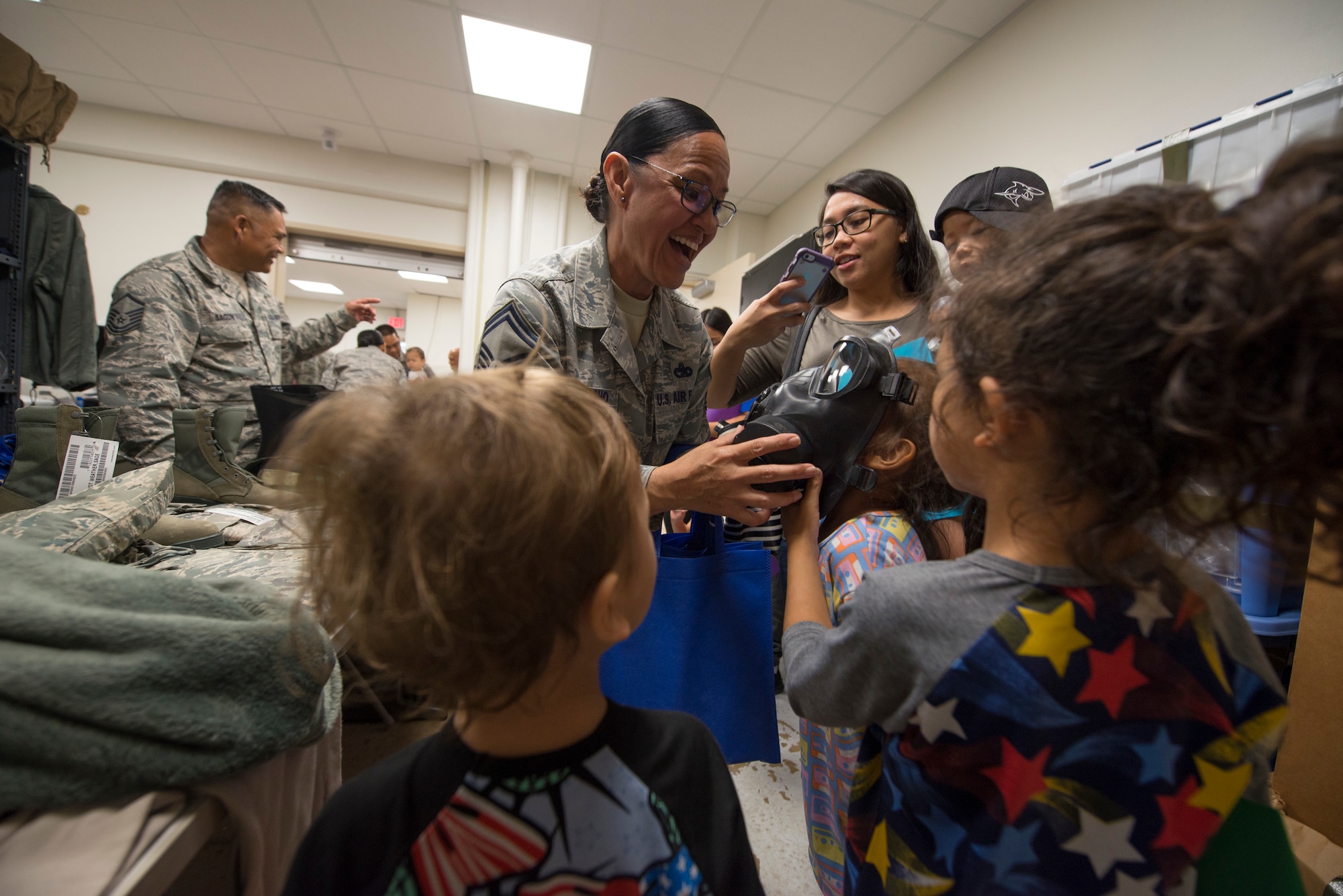 U.S. Air Force Senior Master Sgt. Michelle Quichocho, assigned to the U.S. Air Force Reserve’s 44th Aerial Port Squadron, shows military children a gas mask during Operation Inafa’ Maolek at Andersen Air Force Base, May 5, 2018.