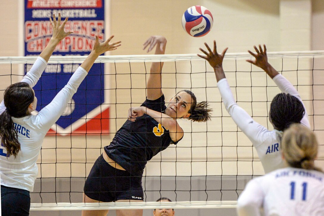 A soldier spikes a volleyball as airmen on the other side of the net raise their arms.