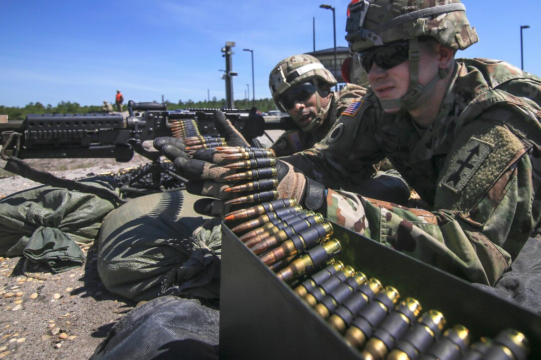 Soldiers load up a belt of ammo before firing a M240B machine gun.