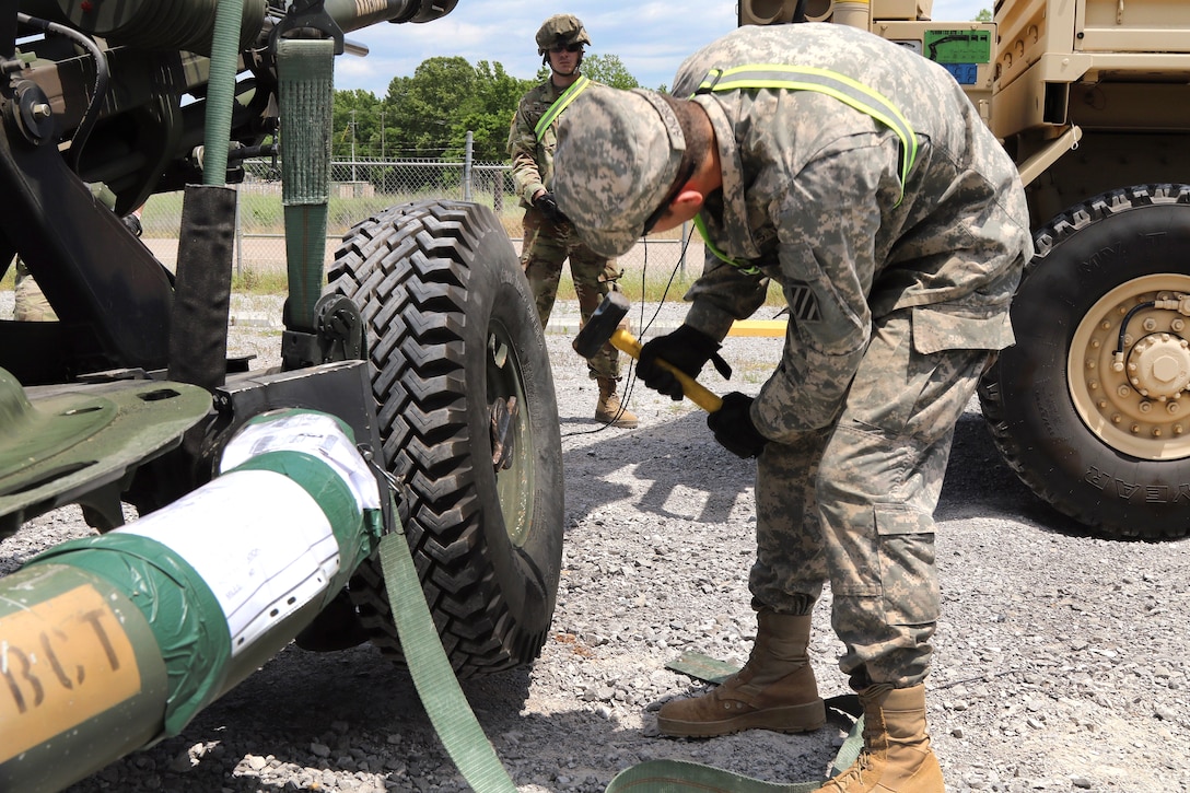A soldier uses a hammer to lock a tire into place on an M119A3 howitzer.