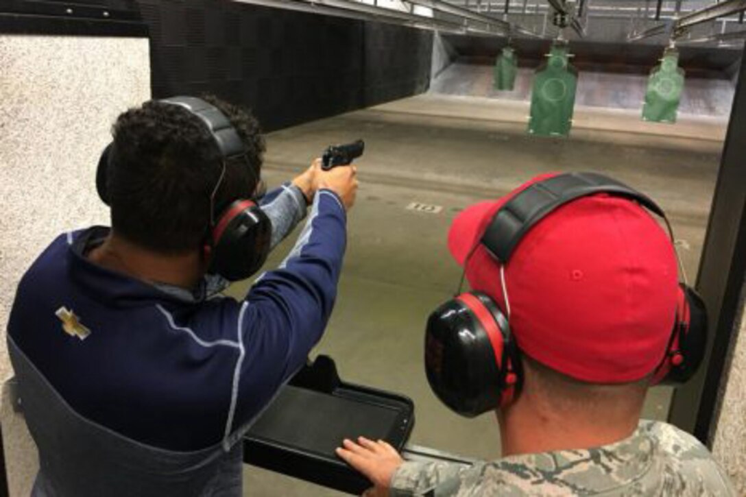 A man shoots a gun at a target while another man watches.