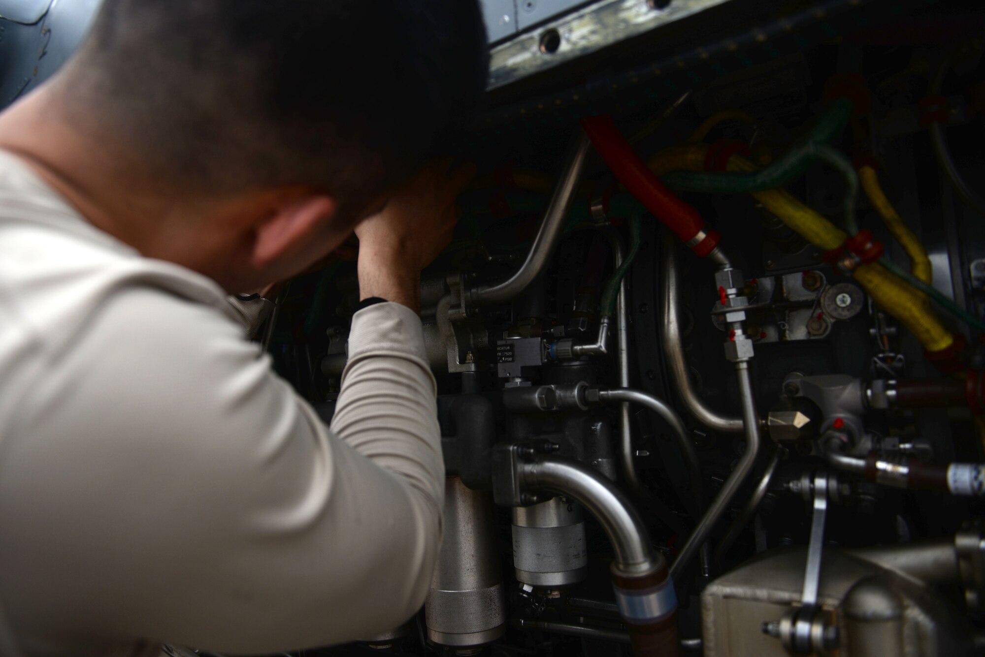 A man in a tan long sleeve shirt reaches in an aircraft engine.