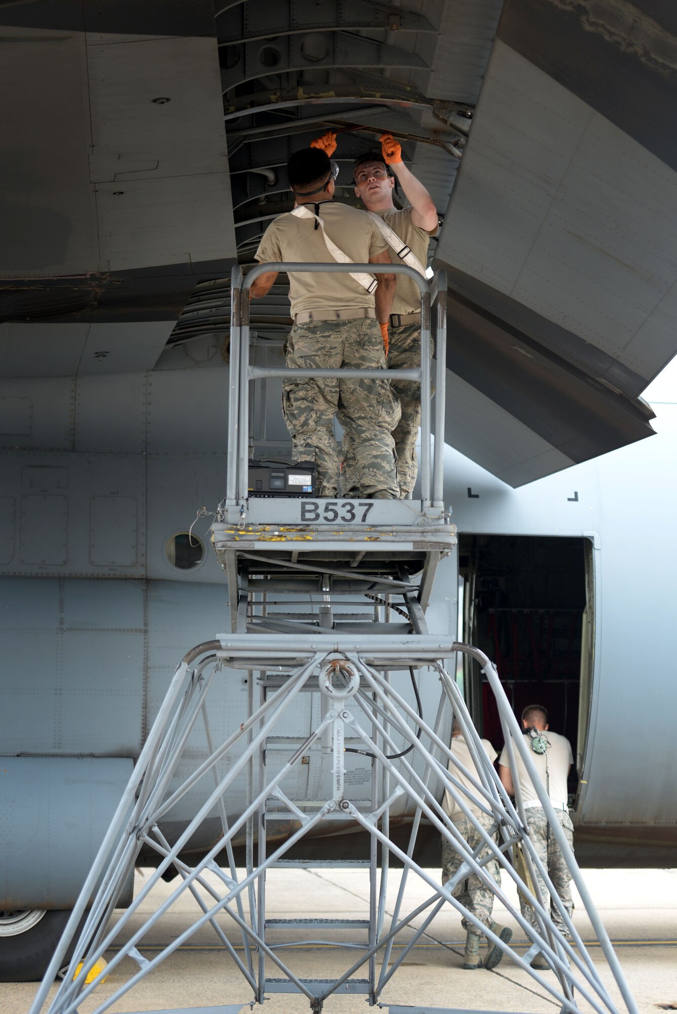 Two men in the Airman Battle Uniform stand on a platform and clean off the inside of a C-130J aircraft wing.