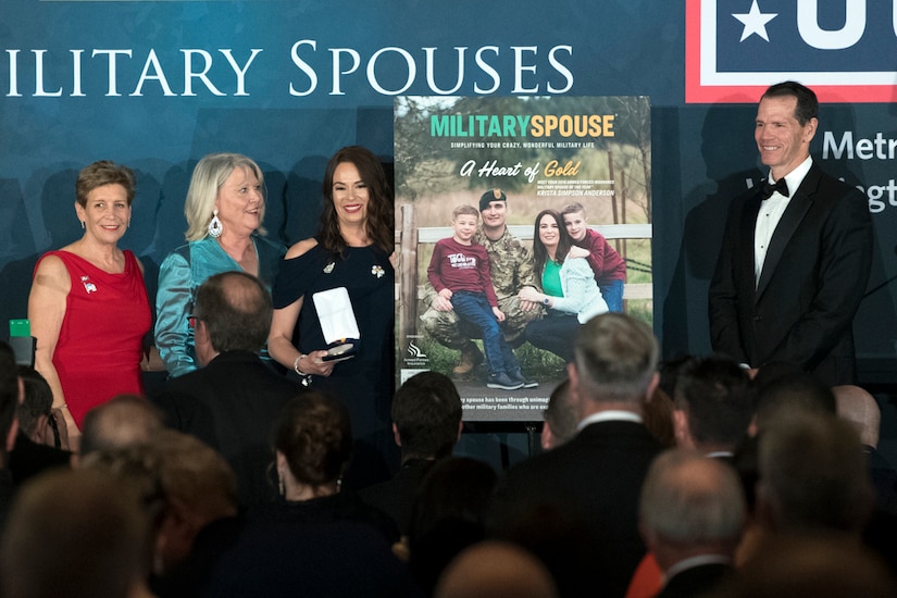 Three women and a man stand around a large poster during the Military Spouse of the Year ceremony.